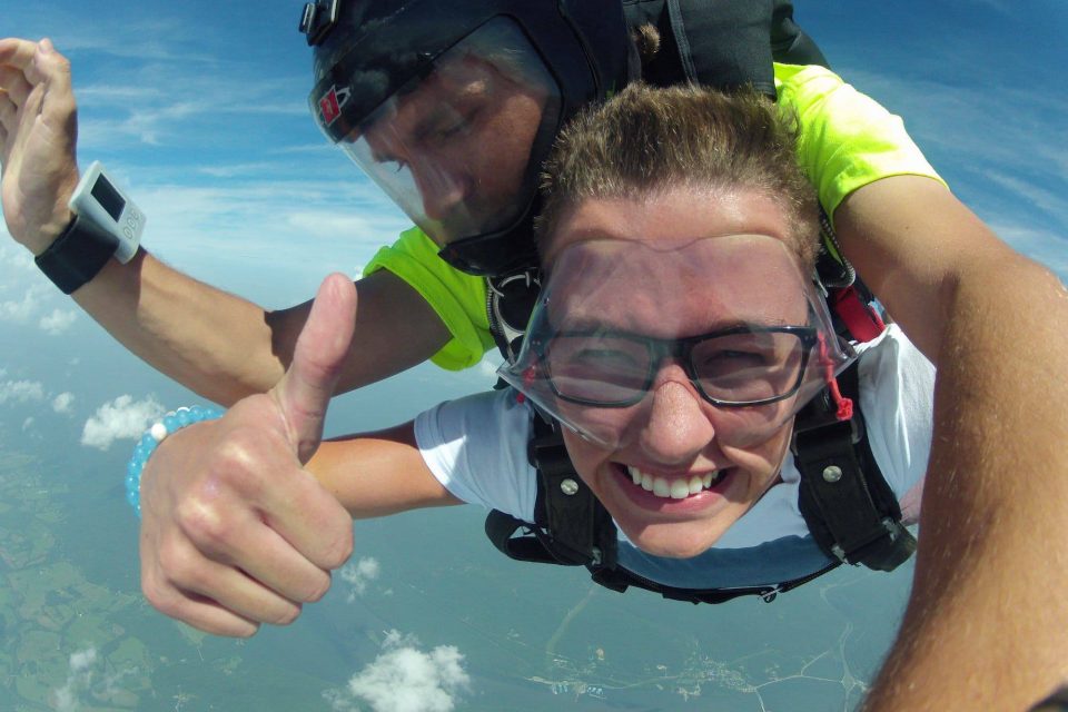 Male tandem skydiver wearing a white shirt giving a thumbs up during freefall