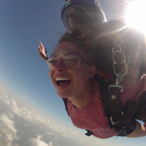 Female tandem skydiver wearing pink shirt smiling during free fall