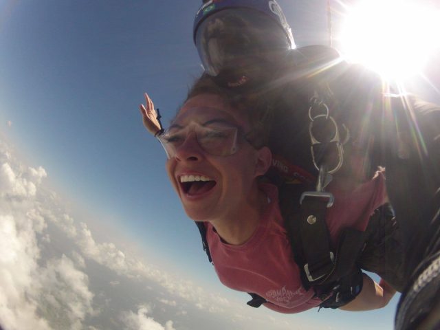 Female tandem skydiver wearing pink shirt smiling during free fall