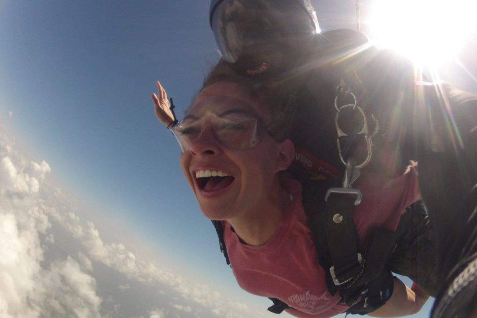 Female tandem skydiver wearing pink shirt smiling during free fall